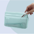 A mint green mesh zippered pouch with a small 'MATCHI' label on the front, shown with a hand inserting a white pen into one of its zip pockets against a pale blue background.
